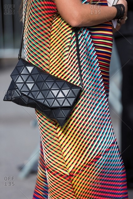 Woman wearing multicolored geometric print dress carrying handbag with triangular quilting