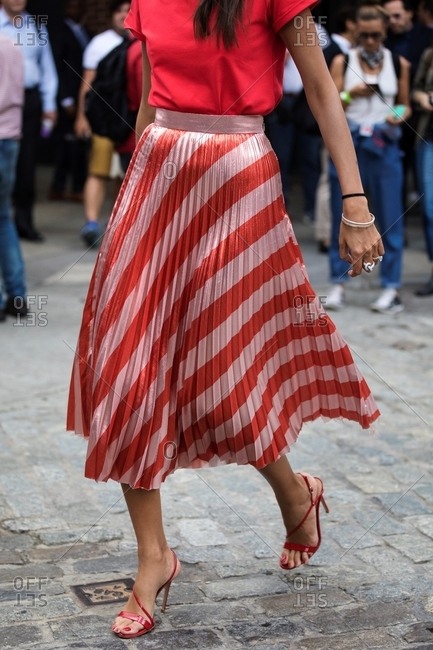 Woman walking wearing long diagonally striped pleated skirt and strappy heels