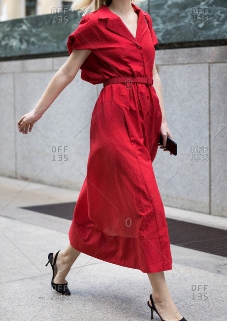Woman striding by wearing scarlet long button up dress with belt