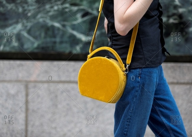 Woman carrying round mustard handbag wearing blue jeans
