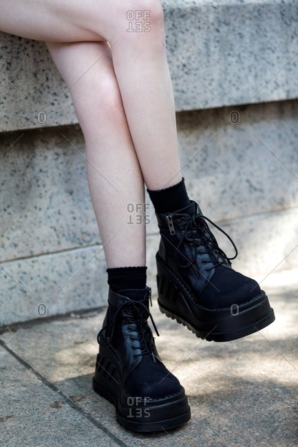 Woman with bare legs sitting wearing black platform boots with zippers