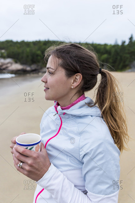 Side view of woman drinking coffee on beach, Acadia National Park, Maine, USA