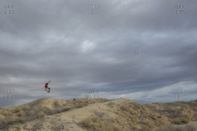 Adult man leaping off top of mound in middle of Anza Borrego State Park badlands, California, USA