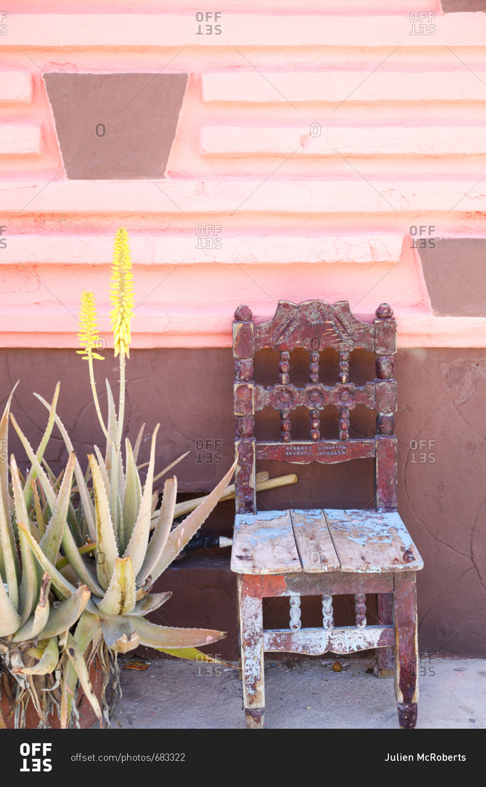 Old weathered chair welcoming people to sit in the shade against pink wall