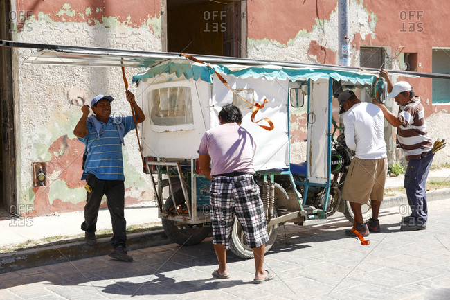 Celestun, Mexico - March 05, 2018: Workers tying down sheets of metal to top of auto rickshaw