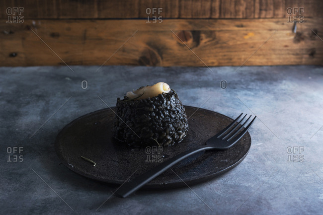 Black rice with cuttlefish, on black cement dish and grunge background