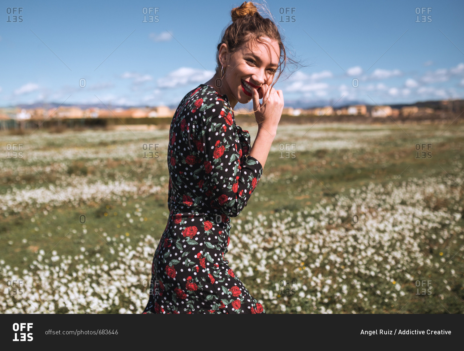 Young attractive woman standing on field with small flowers and looking at camera.