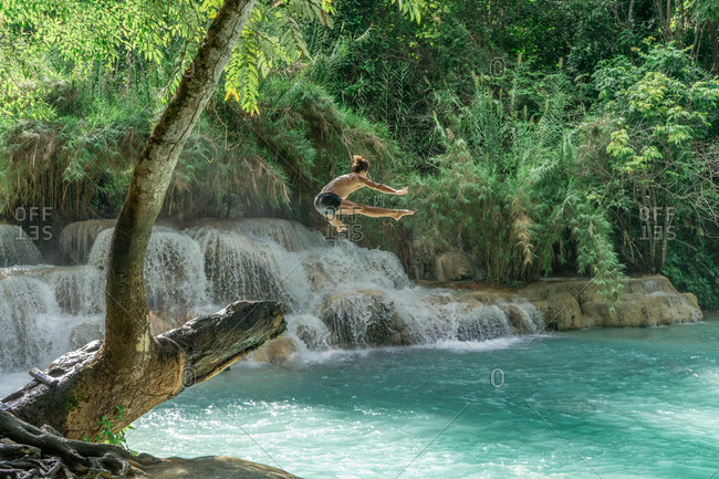 Unrecognizable man jumping high to turquoise water at the waterfall.