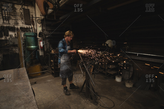 Blacksmith grinding a metal rod with grinder machine n workshop