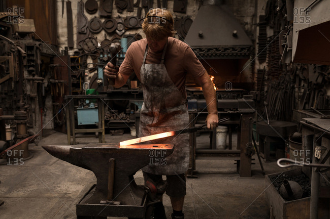 Blacksmith hammering a hot metal rod in workshop