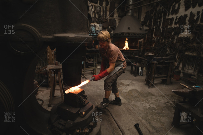 Blacksmith shaping hot metal rod in machine at workshop
