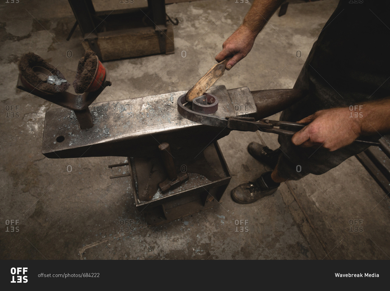 Blacksmith using hand wire brush on metal rod in workshop