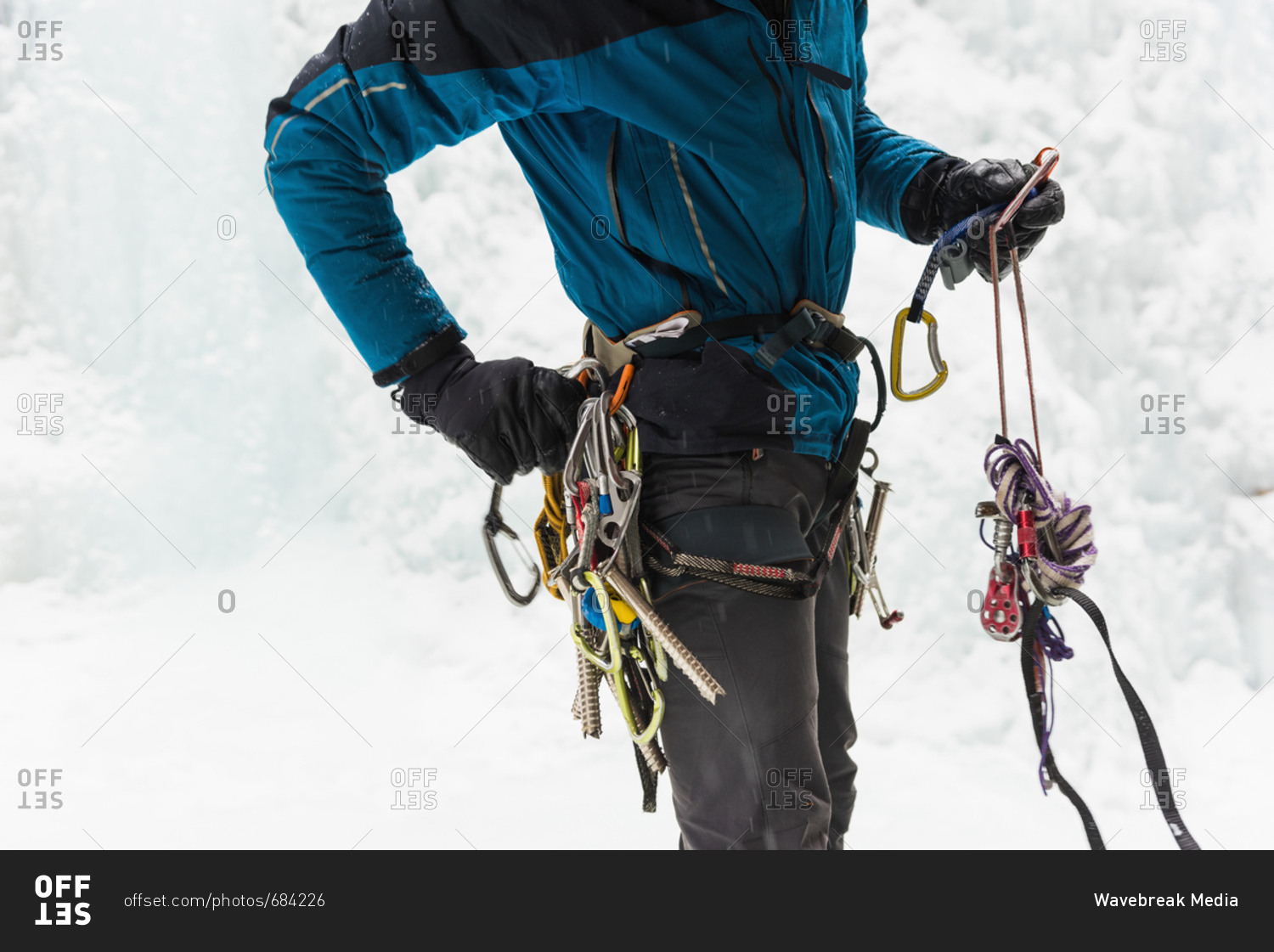 Mid section of male rock climber wearing harness near rocky mountain during winter