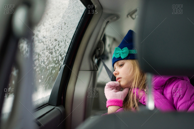 Girl passenger peering curiously out frosted car window