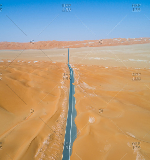 Aerial view of an empty straight road covered by sand in the desert of Abu Dhabi, UAE