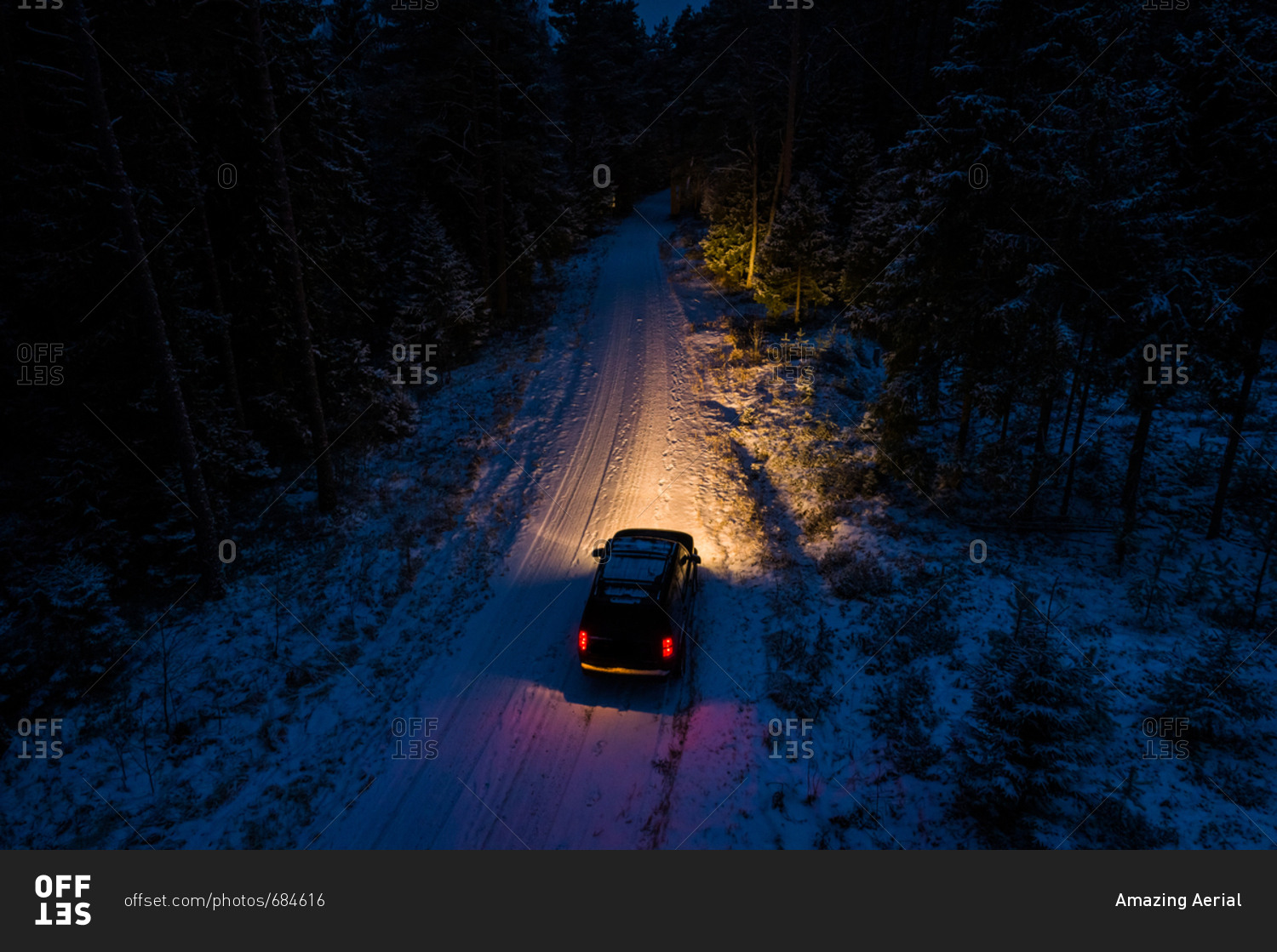 Aerial view of a car driving by night on the snowy road in the forest