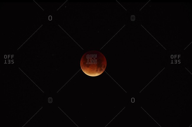 Long exposure showing a  red tinged moon with the majority in shadow during a full  lunar eclipse