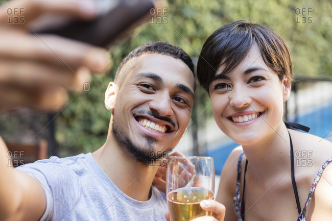 Smiling young couple having a beer and taking a selfie outdoors