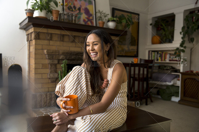 Laughing young woman with coffee mug sitting at home