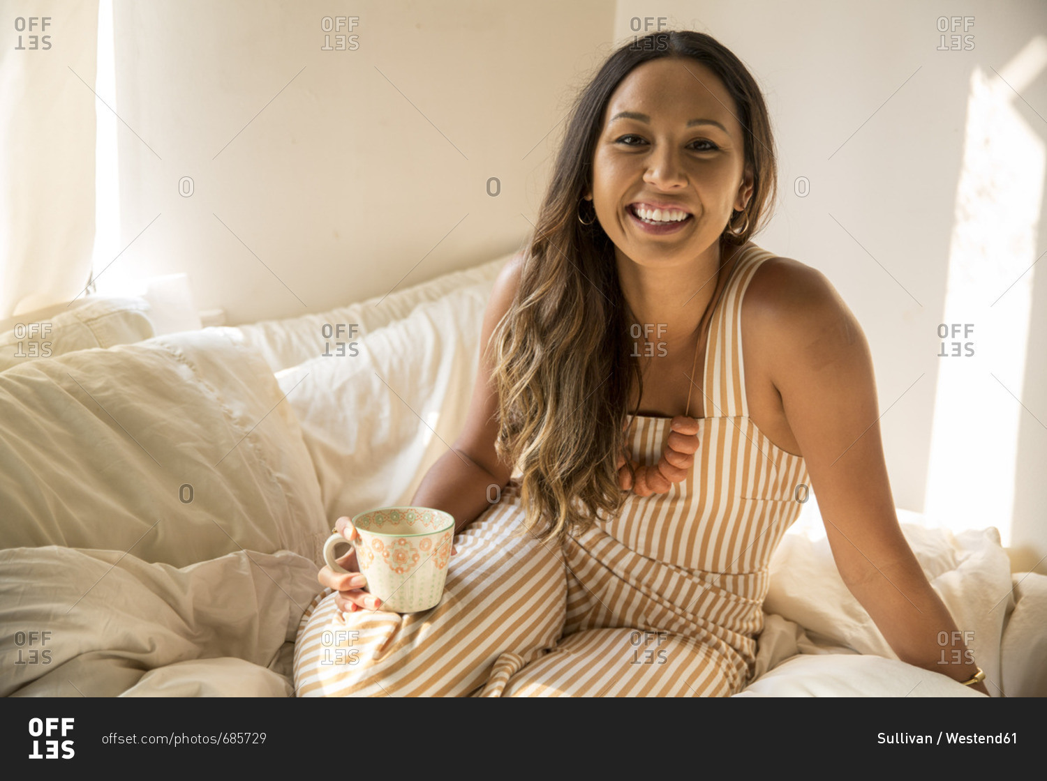 Portrait of happy young woman with coffee cup in bed