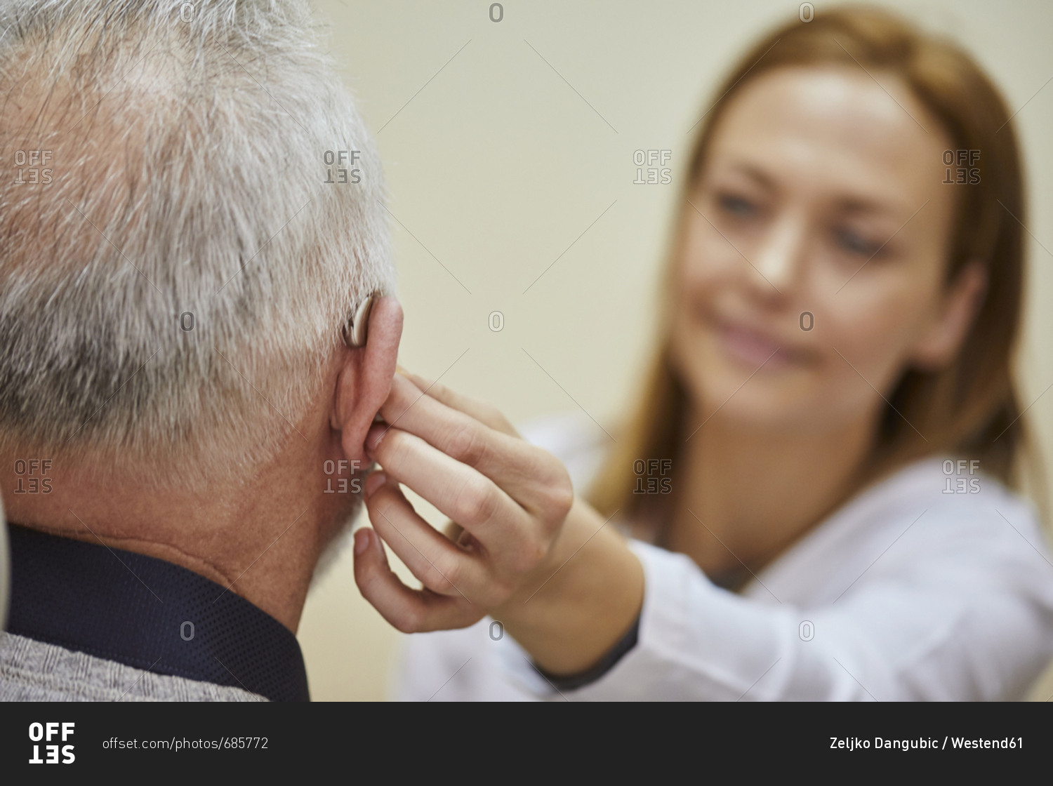 Female doctor applying hearing aid to senior man's ear stock photo OFFSET