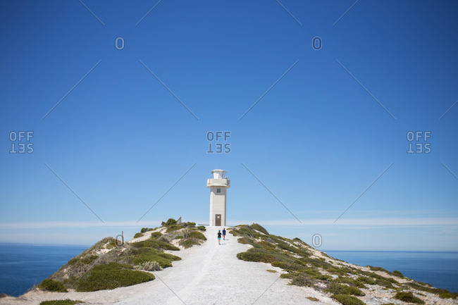 Two people hiking toward lighthouse at top of coastal headland
