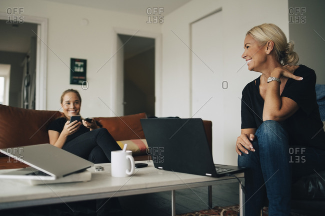 Smiling teenage girl and mother sitting with laptops on coffee table in living room at home