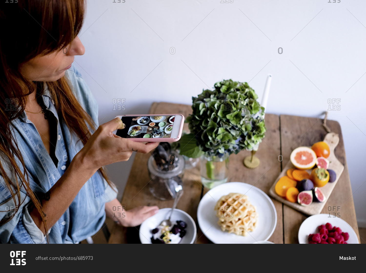 High angle view of female blogger photographing food at table through mobile phone by wall