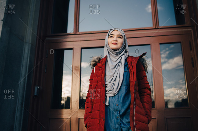Low angle view of confident young Muslim woman standing against entrance door in city