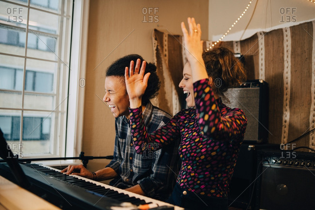 Happy friends enjoying while playing piano and practicing at recording  studio stock photo - OFFSET