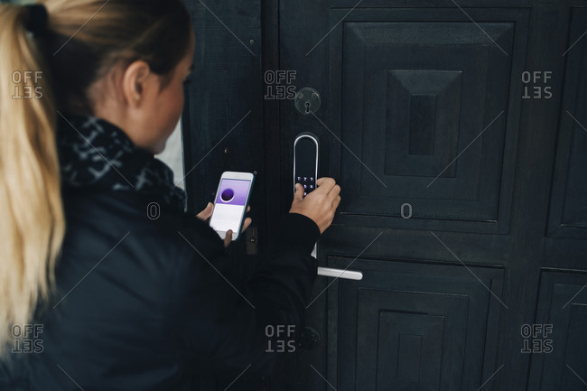 Rear View Of Teenage Girl Using Smart Phone To Unlock House