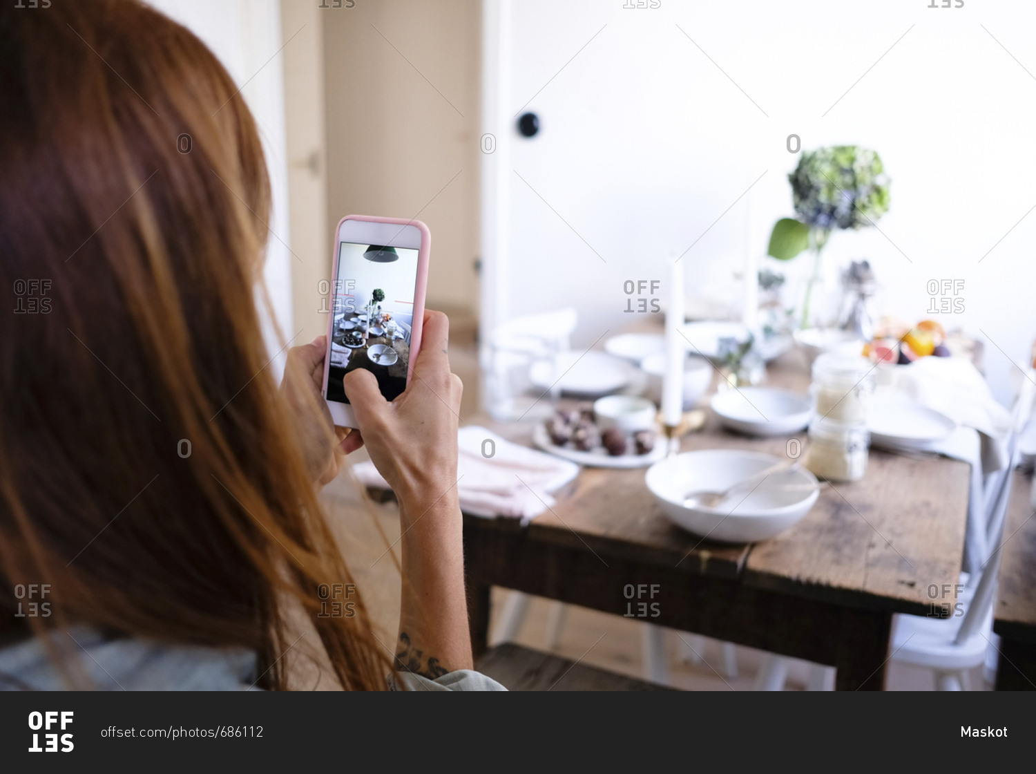 Rear view of woman photographing plates and food on table by wall at home