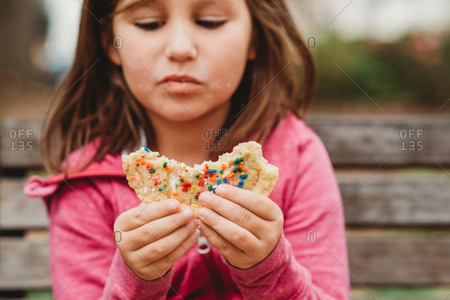 Young girl enjoying large cookie on park bench