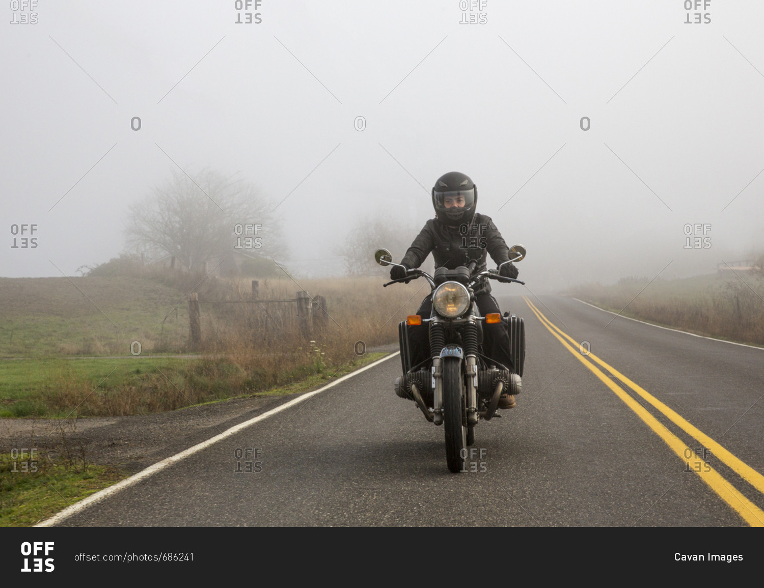 Female biker riding motorcycle on country road during foggy weather