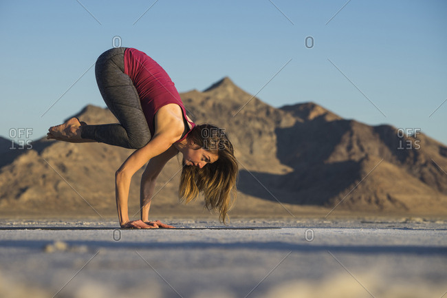 Side view of woman practicing crow pose against clear blue sky during sunset