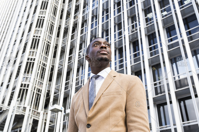 Low angle vie of young black professional man staring off camera in front of building