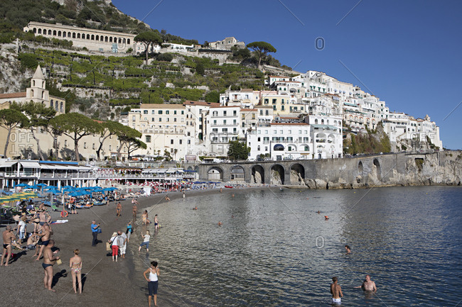 Amalfi Coast, Italy - October 20, 2017: Tourists on beach beneath village along the Amalfi Coast of Italy