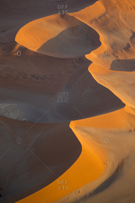 Africa, Namibia, Namib Naukluft National Park, Aerial view of morning sun lighting windblown red sand dunes in Namib Desert near Sossusvlei