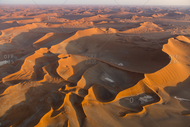 Africa, Namibia, Namib Naukluft National Park, Aerial view of morning sun lighting windblown red sand dunes in Namib Desert near Sossusvlei