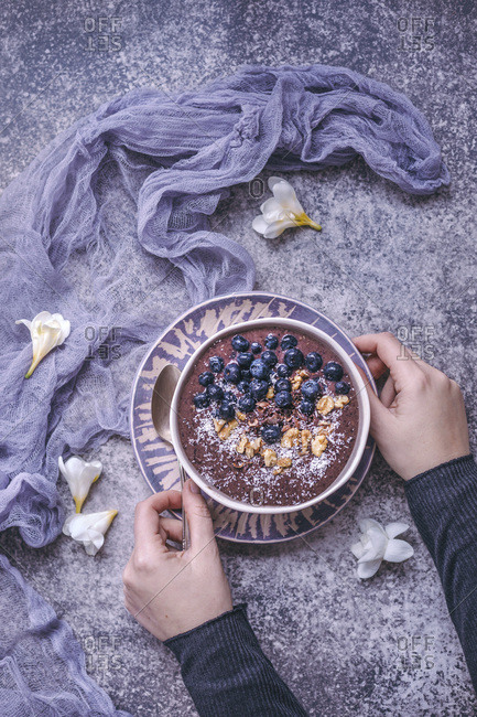 Woman eating blueberry smoothie bowl topped with blueberries, walnuts, cacao nibs and coconut