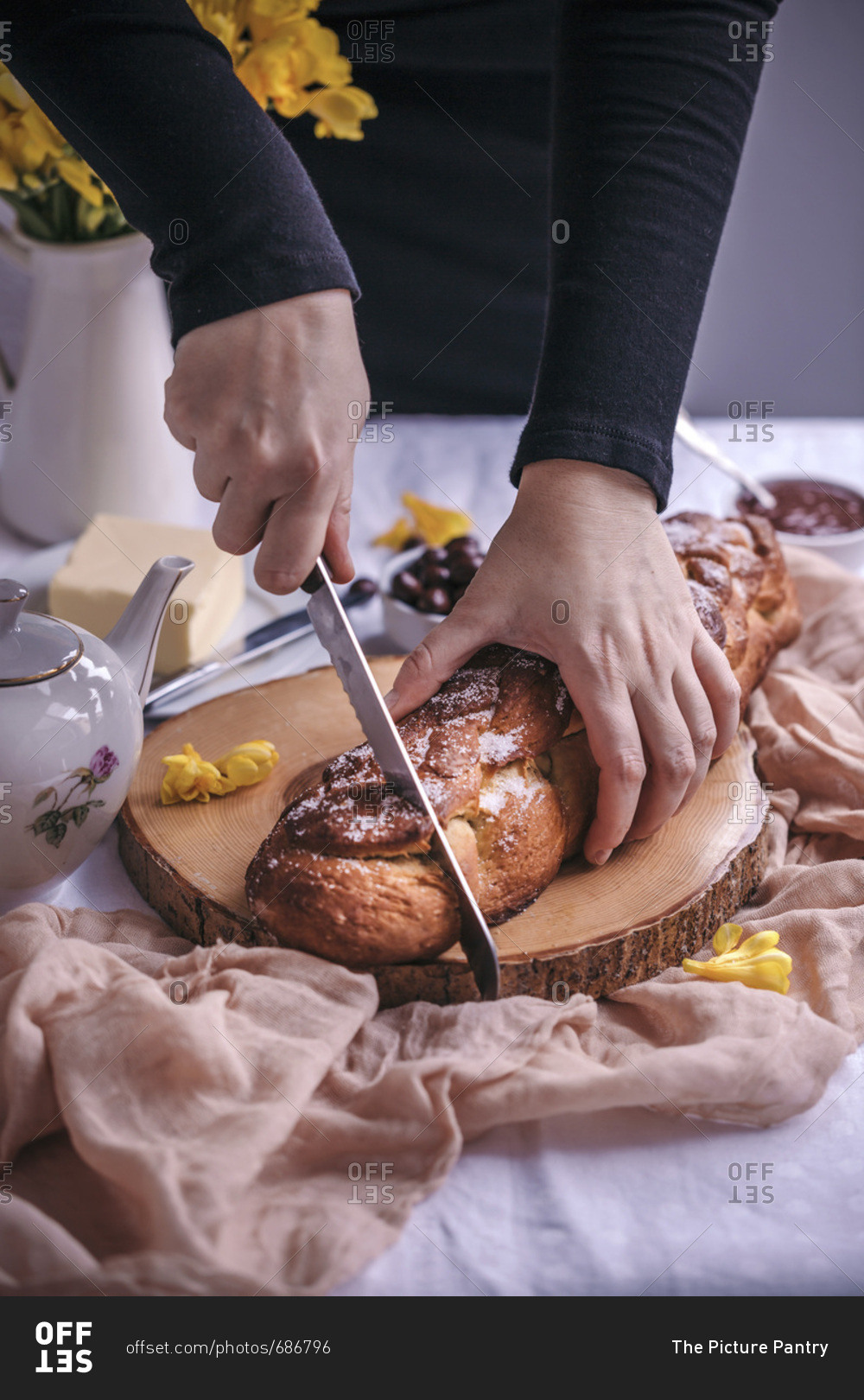 Woman slicing braided sweet Easter bread served for breakfast with butter and jam