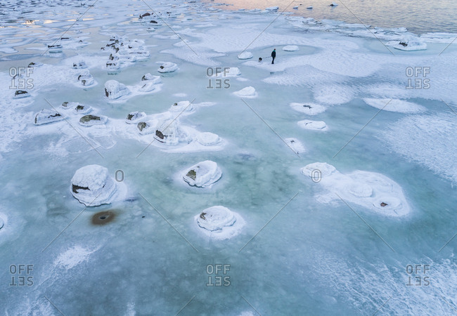 Aerial view of a man walking his dog on the frozen sea in Muraste, Estonia