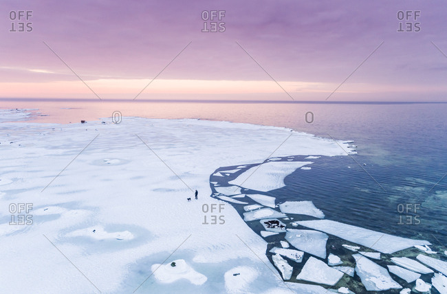 Aerial view of a man walking his dog on the frozen sea in Muraste at sunset, Estonia