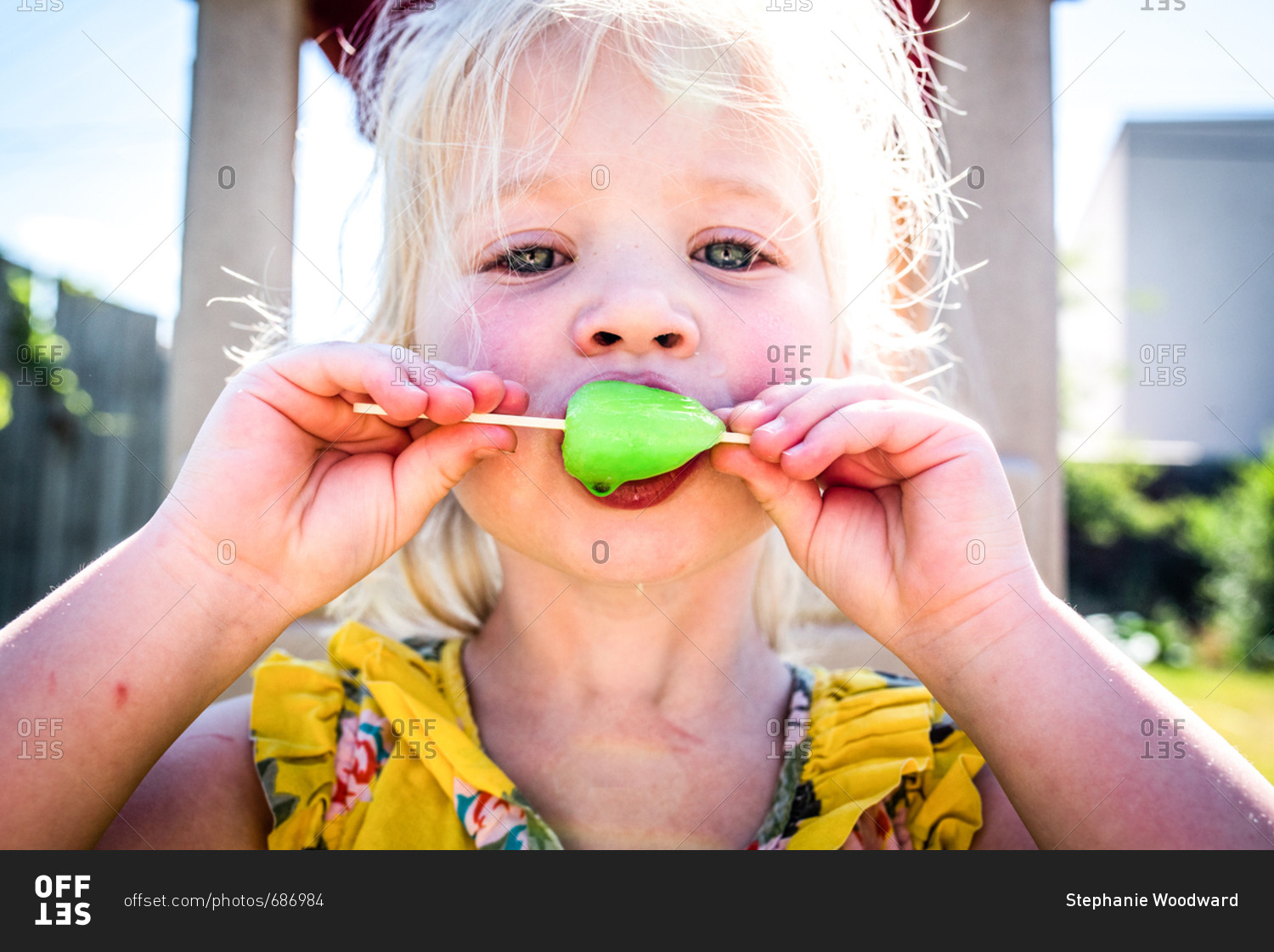 Little girl eating neon popsicle on summer day