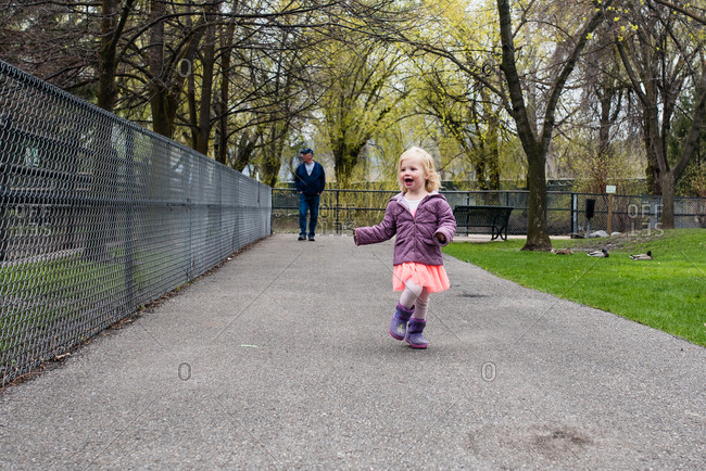 Girl walking on path at the zoo with grandfather trailing behind