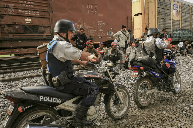 Celaya, Mexico - November 08, 2007: Armed police on motorbikes ride by group of migrants sitting on train tracks hoping to get to border with United States of America