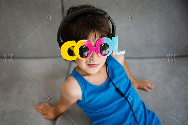 Portrait of little boy on couch wearing novelty sunglasses and headphones