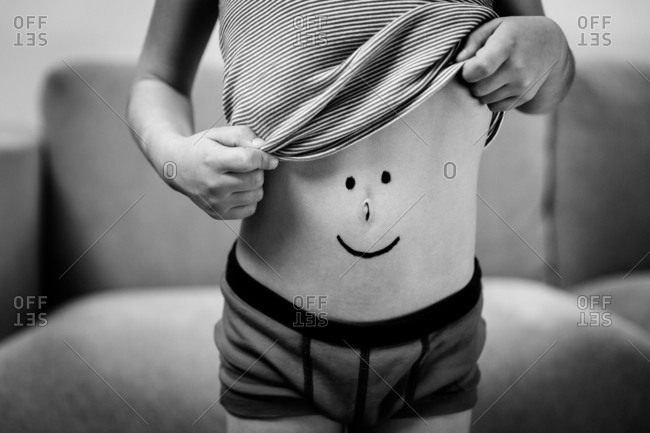 Little boy lifting t-shirt to show smiley face drawn on belly