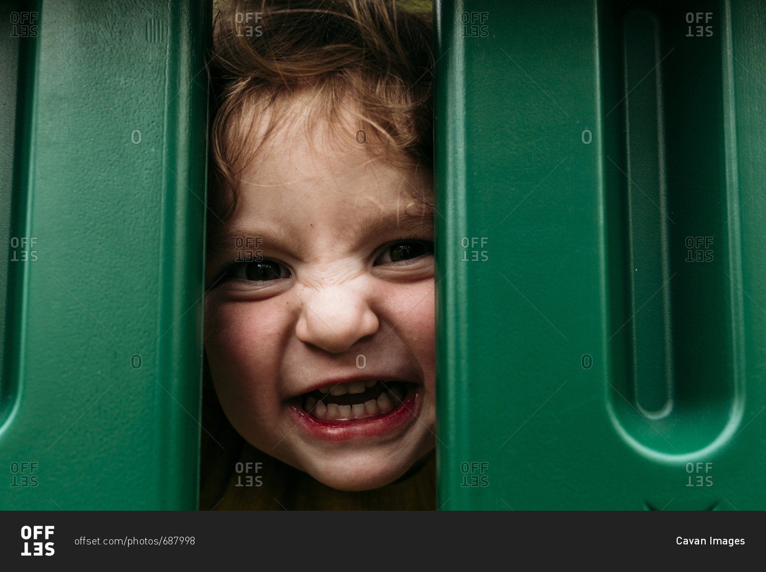 Portrait of cute playful girl making face while peeking through outdoor play equipment