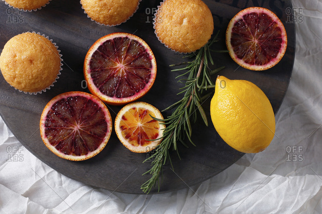 High angle view of fairy cakes with rosemary and citrus fruits on cutting board